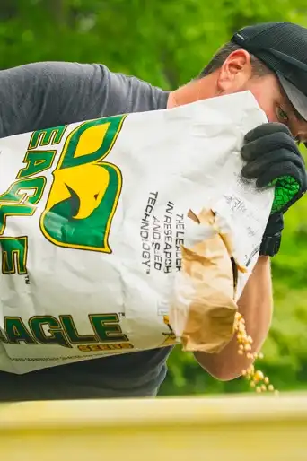 man poring a bag of see into a planter